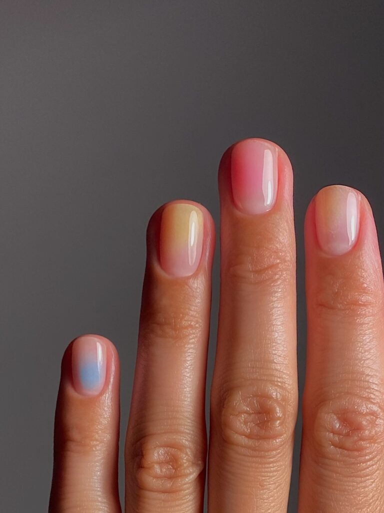 Short airbrush aura nails with soft pastel gradients of pink, yellow and blue
