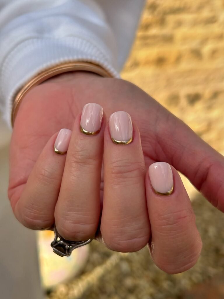 Short milky pink nails with thin gold french tips, an elevated classic french manicure