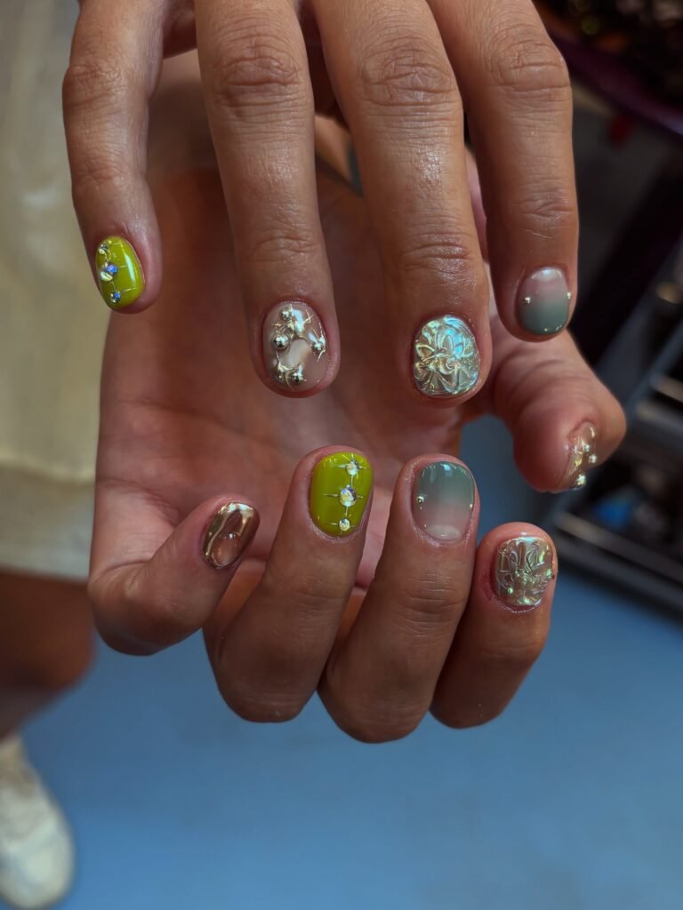 Short maximalist nails with chrome details, rhinestones and 3D charms in green and sage shades