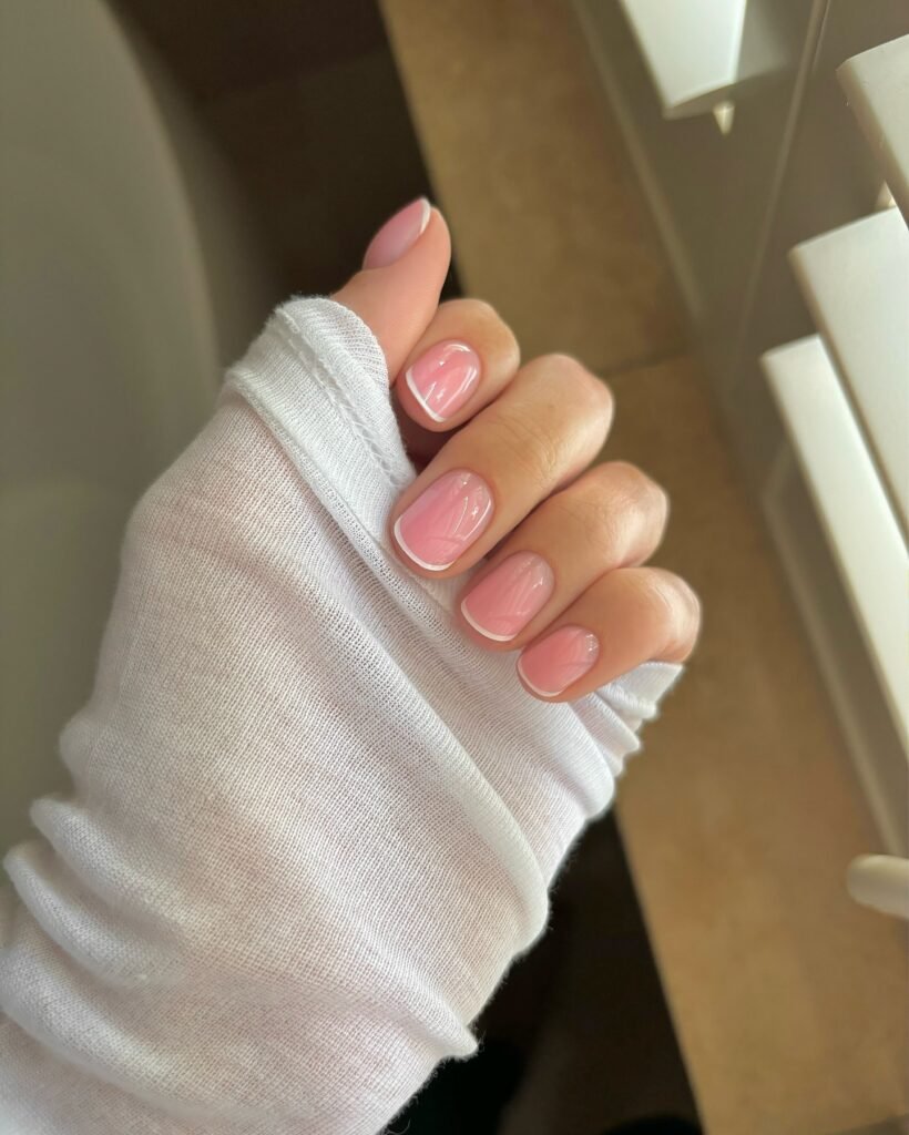 Short pink french nails with thin white tips on a sheer glossy pink base