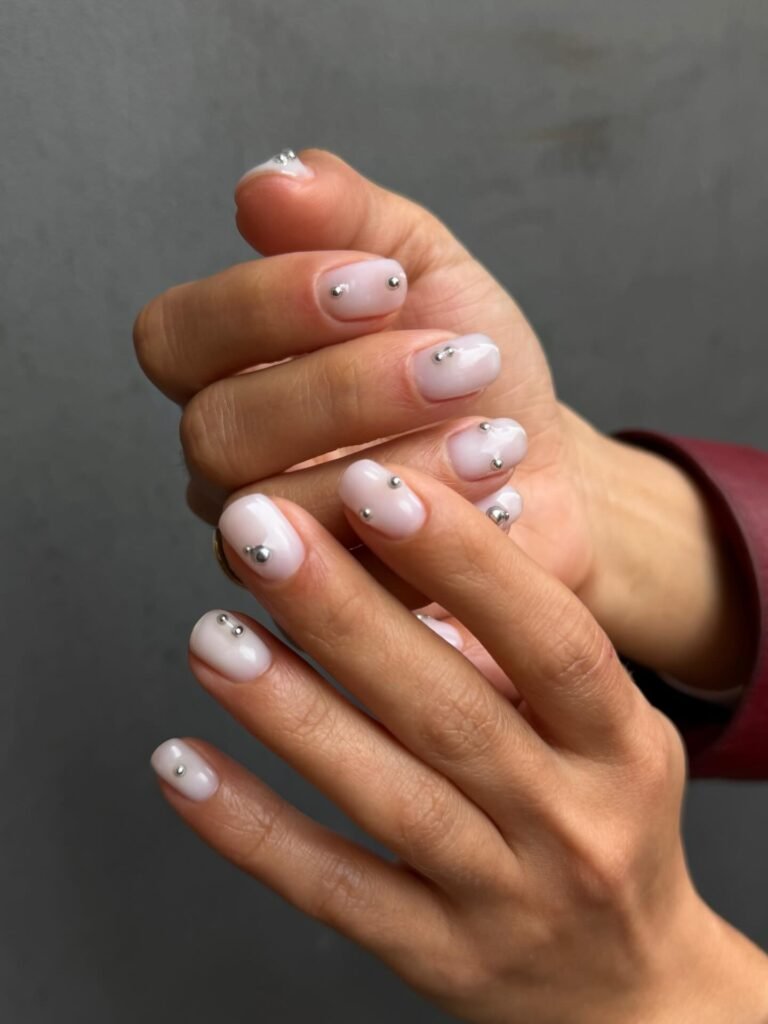 Short white nails with tiny silver stud accents, a minimalist chrome detail manicure