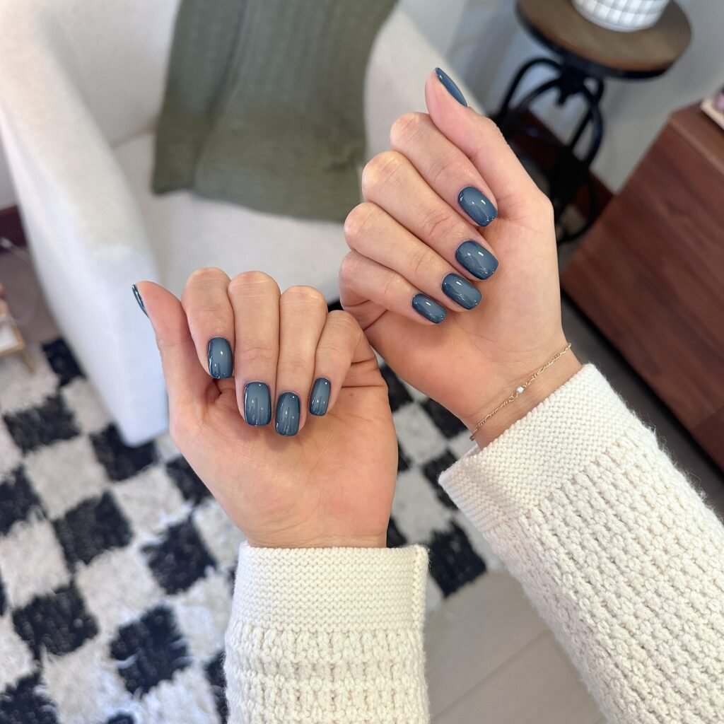 Dusty denim blue nail polish on long squoval nails, a slate blue-grey fall manicure worn with a cream sweater.