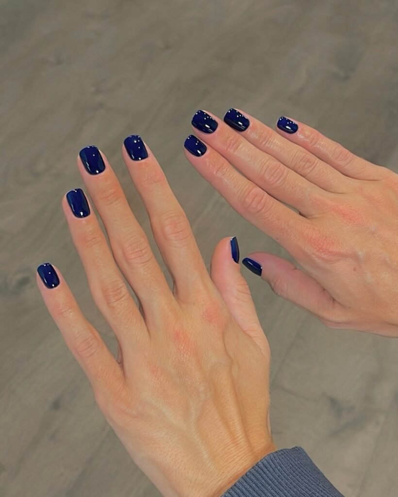 Glossy midnight blue nail polish on short square nails, a deep navy fall 2026 manicure trend.